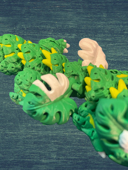 1 Layer At A time Baby Monstera Plant Dragon, a green and yellow articulated 3D printed dragon with monstera leaf details and white accents.
