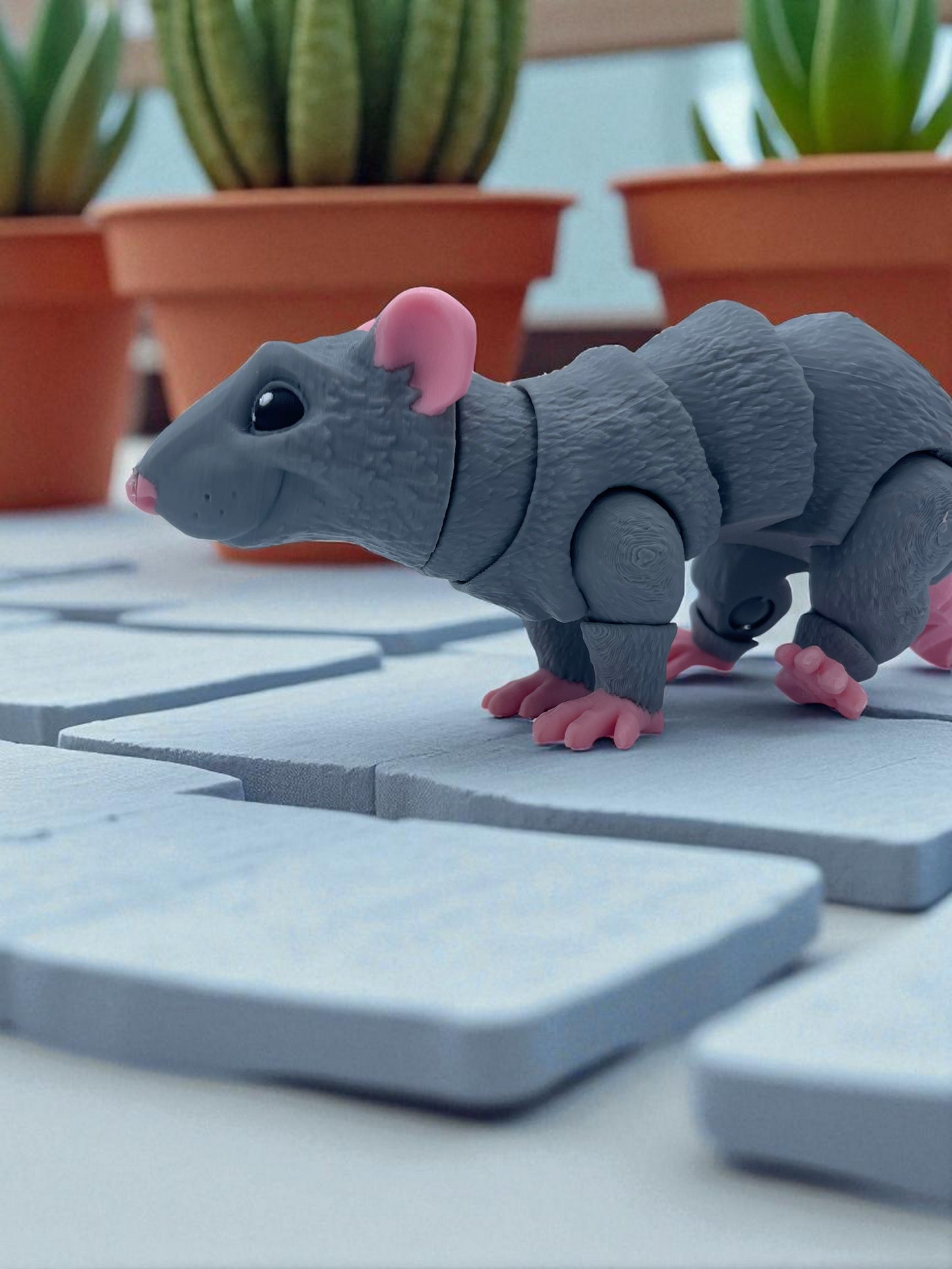 Gray toy rat on a stone surface with potted plants in the background