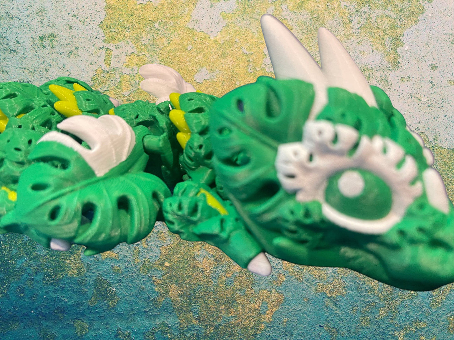 1 Layer At A time Baby Monstera Plant Dragon, a green articulated 3D printed dragon with monstera leaf details and white accents.