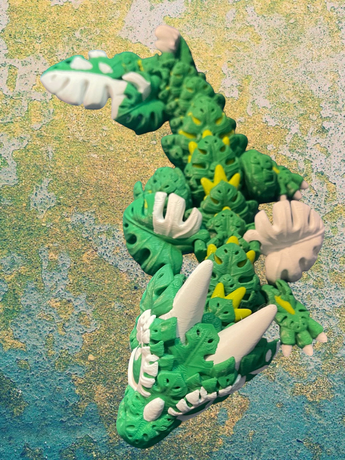 1 Layer At A time Baby Monstera Plant Dragon, a green and white articulated 3D printed dragon with monstera leaf details.