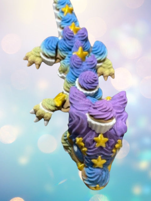 1 Layer At A time Birthday Cupcake Dragon with articulated body, poseable legs, and clicker tail. Multi-colored with purple, blue, yellow, and green icing swirls and yellow stars.