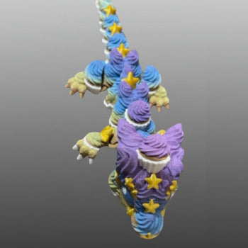 1 Layer At A time Birthday Cupcake Dragon with articulated body, poseable legs, and clicker tail. Multi-colored with purple, blue, yellow, and green icing swirls and yellow stars.