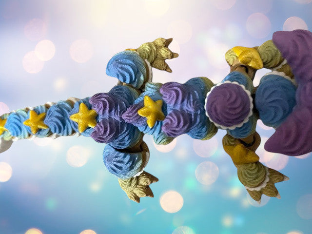 1 Layer At A time articulated 3D printed dragon toy with cupcake frosting texture, blue, purple, yellow, and green colors, and yellow stars.