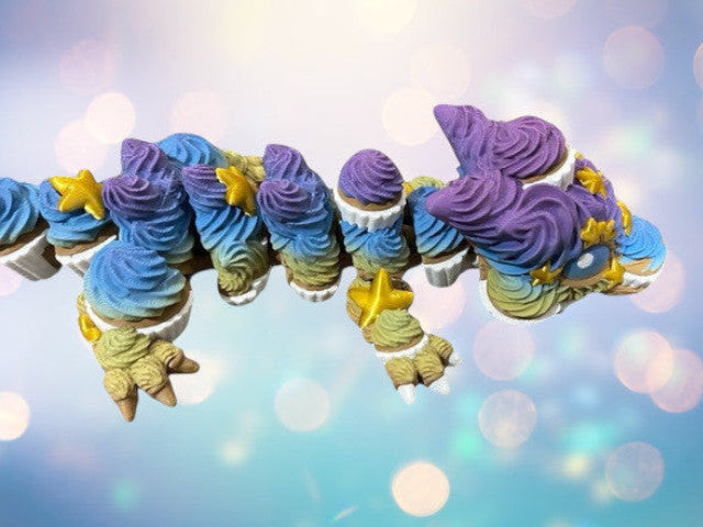 1 Layer At A time articulated cupcake dragon with blue, purple, and yellow frosting details and gold stars.