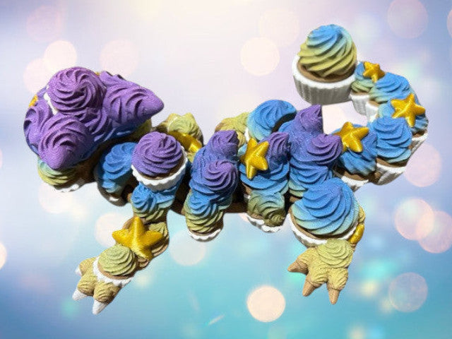 1 Layer At A time articulated 3D printed cupcake dragon toy with purple, blue, and yellow frosting details and gold stars.