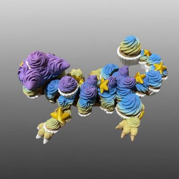 1 Layer At A time articulated 3D printed cupcake dragon toy with purple, blue, and yellow frosting details and gold stars.