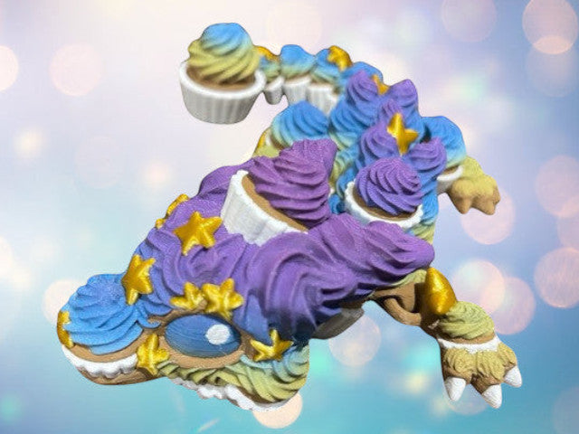 1 Layer At A time 3D printed cupcake dragon with purple, blue, and yellow frosting details and gold stars.
