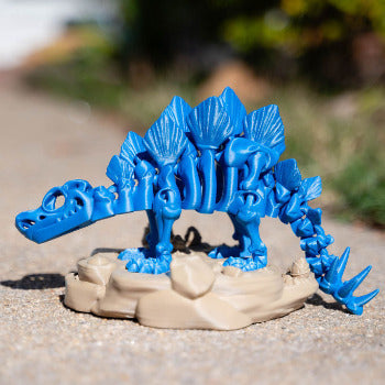 Blue dinosaur toy figure on a beige base outdoors