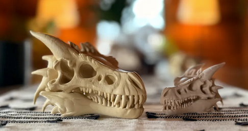 Two dragon skull models on a textured surface with a blurred background